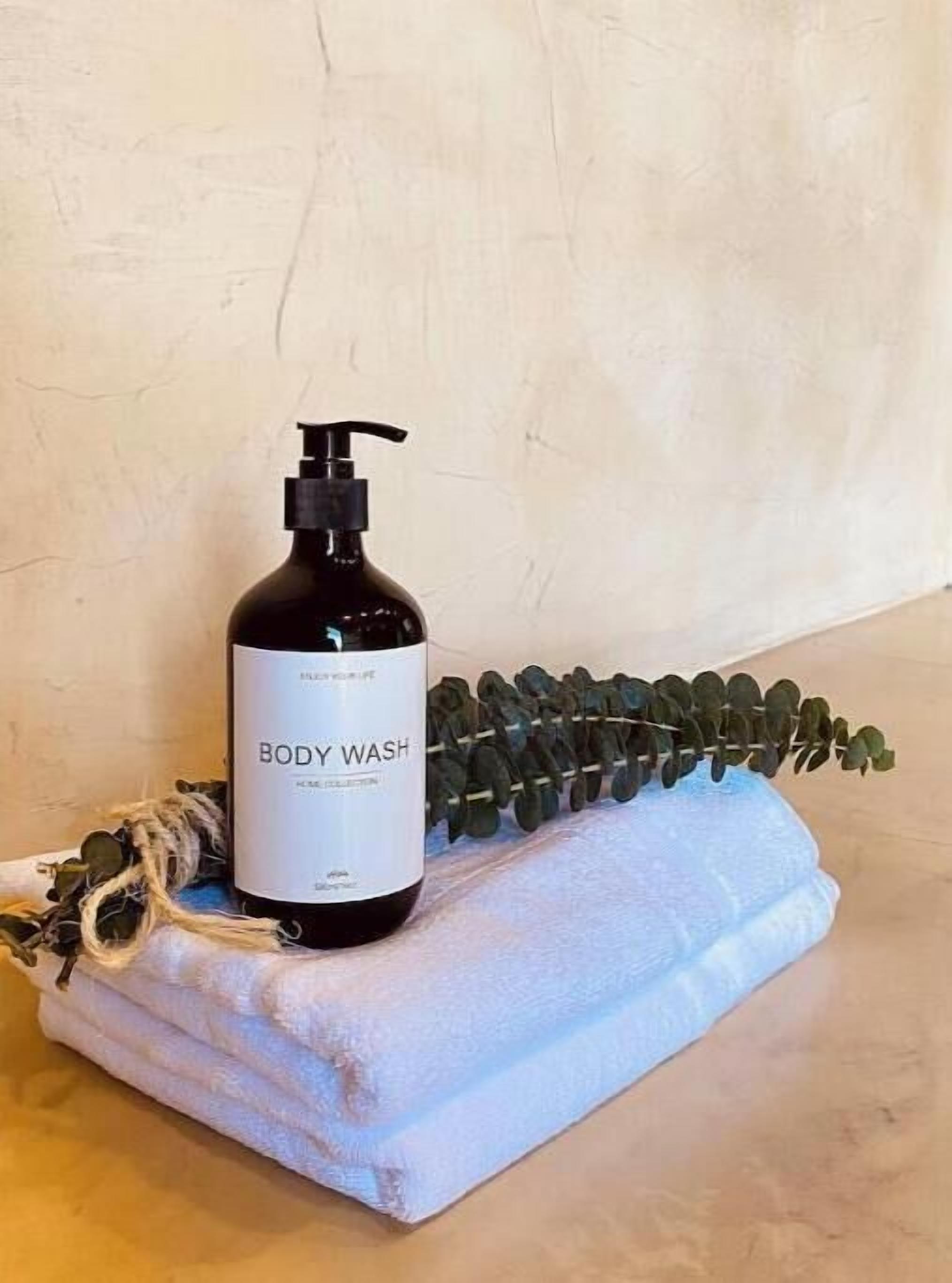 A bottle of body wash on a towel with a plant beside it.