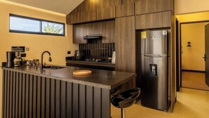 A modern kitchen with dark wood cabinetry, a stainless steel refrigerator, and a built-in island with a sink and seating.
