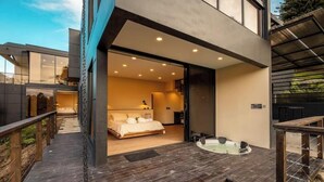 A modern bedroom with a large bed, a private bathroom, and a hot tub on a wooden deck.