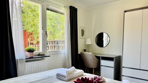 A hotel room with a bed, a desk, a chair, a window with curtains, a potted plant, a lamp, and a mirror. - Brilliant family getaway in Stockholm - 4 Guests (Kista)