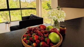 Une table sur laquelle se trouve un panier en osier rempli de fruits (fraises, raisins et pommes), un vase avec des fleurs blanches et un pot de confiture.