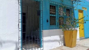A building with a blue and white facade, a yellow door, and a large planter with a plant. - Room for 2 people in Playa Salguero (Gaira)