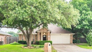 A single-story house with a brick facade, a garage, and a large tree in front. - Cozy Corner Near I-20 & 360, Heart of DFW, Quiet Cul-de-Sac Stay (Arlington)