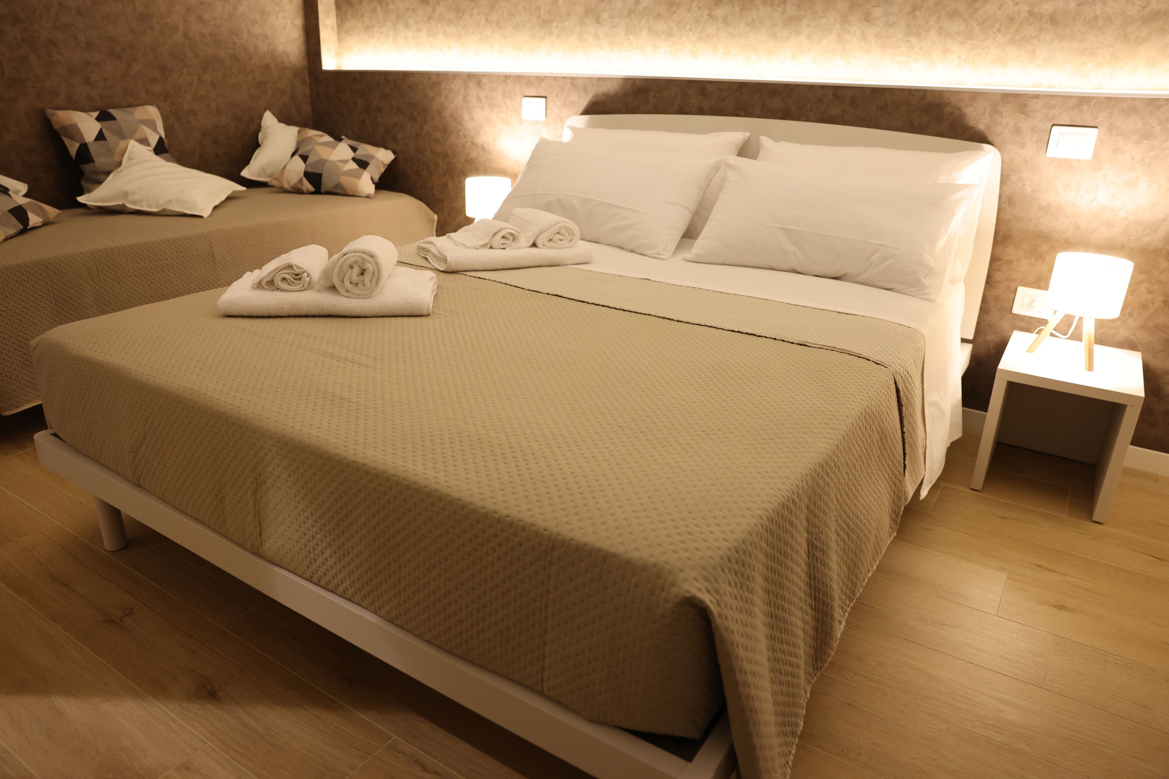 A hotel room with two beds, each with a beige bedspread and white pillows. There are two bedside tables with lamps.