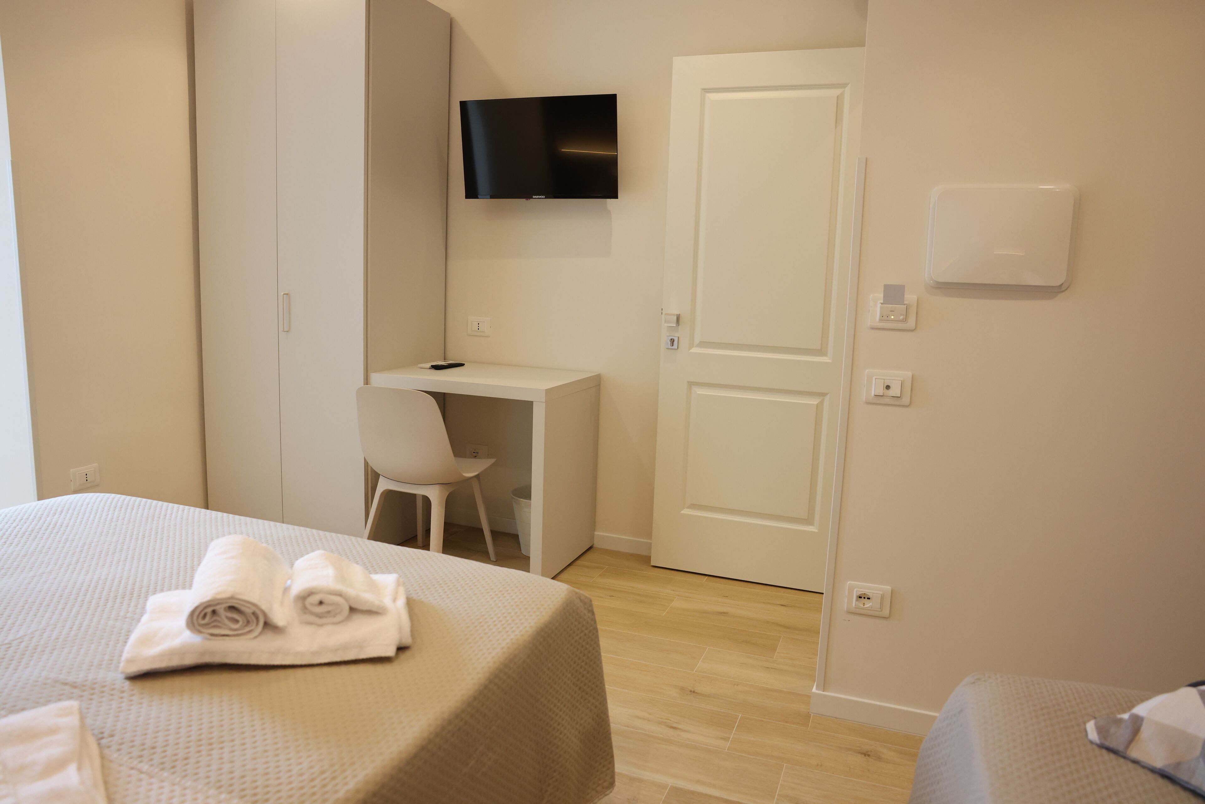 A hotel room with a bed, a desk, a chair, a television, and a door.
