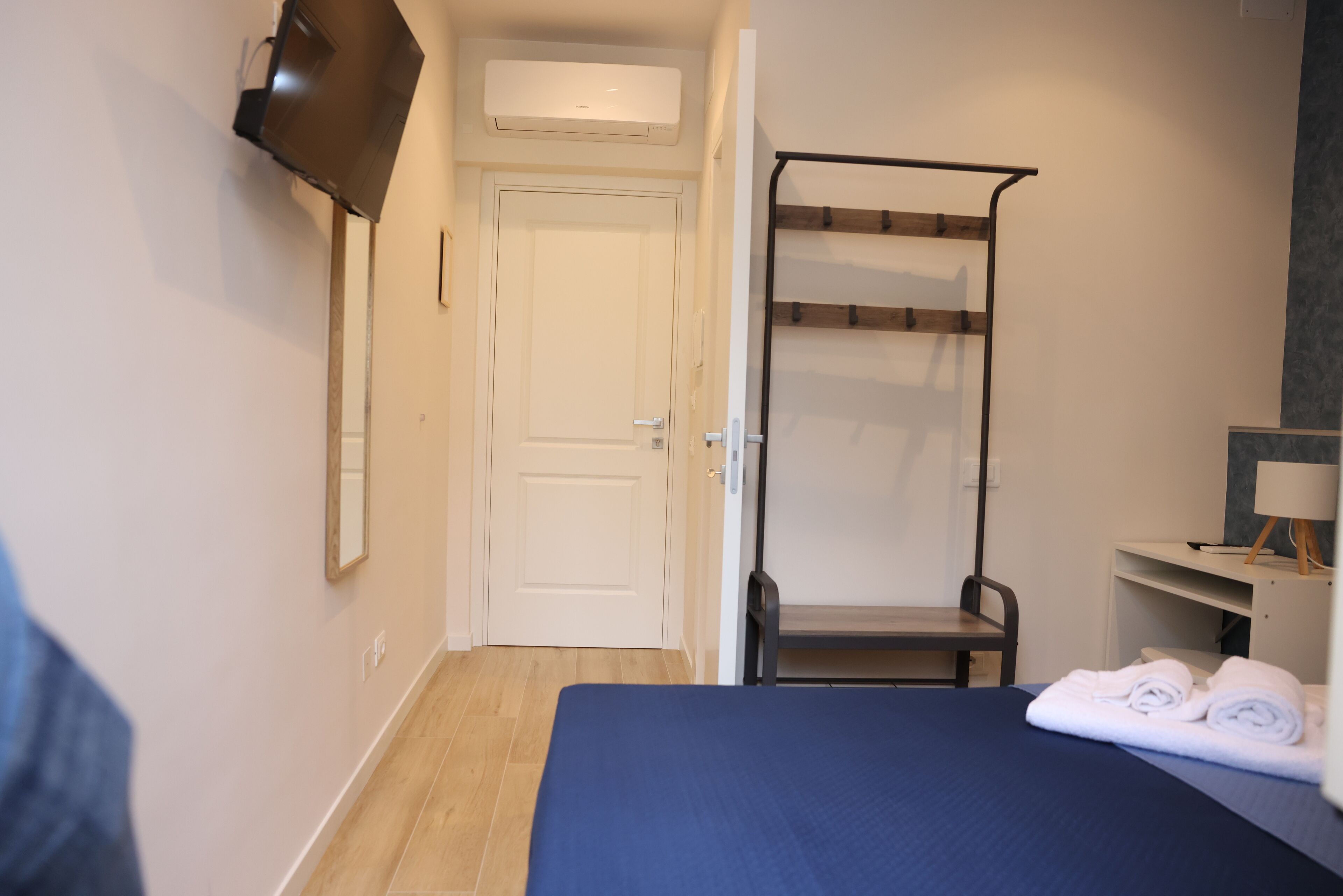 A hotel room with a bed, a desk, a chair, a TV mounted on the wall, and a door.