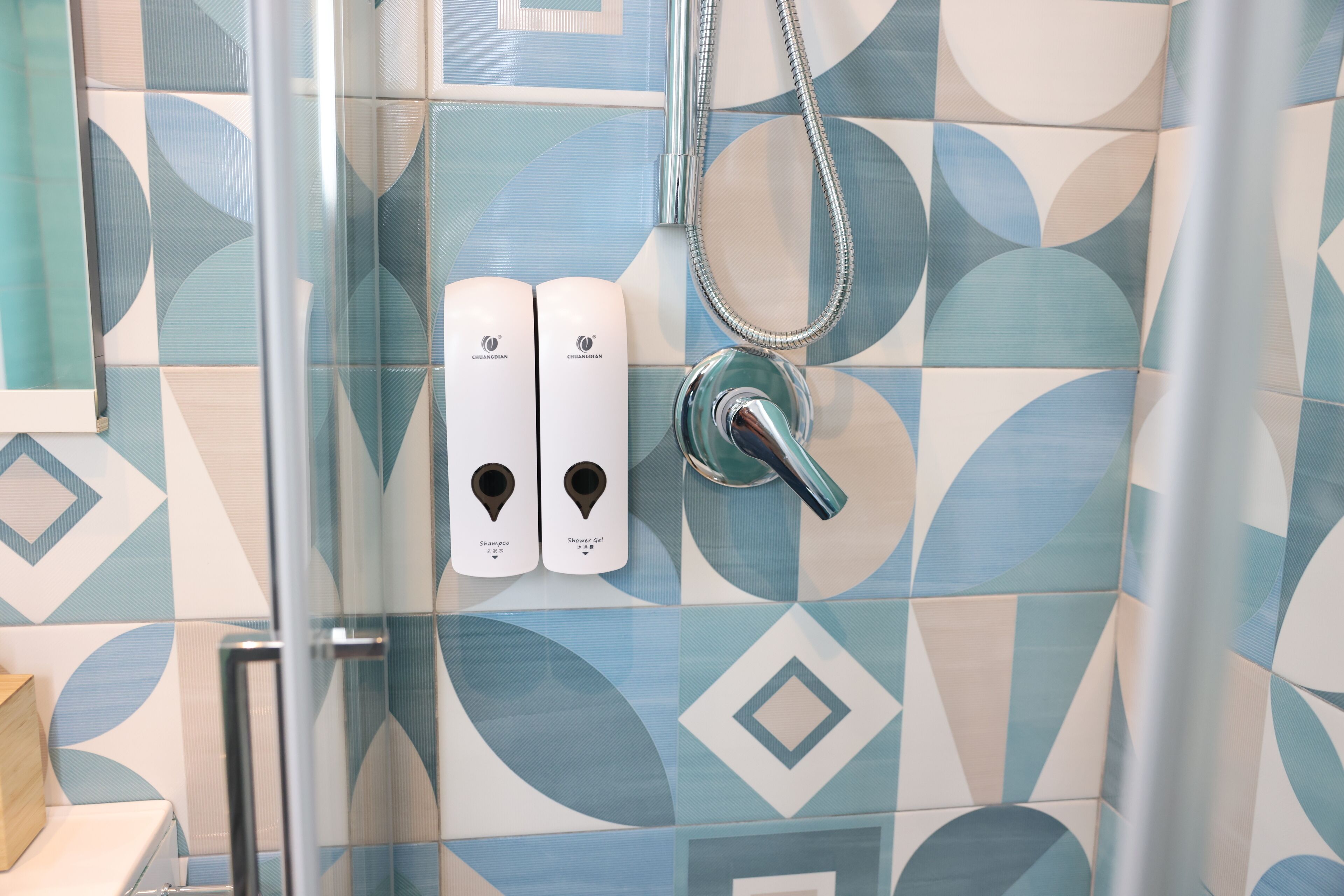 A bathroom with a shower, a glass door, and two soap dispensers on the wall.