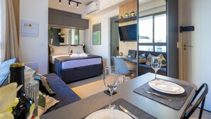 A modern hotel room with a bed, a dining area with a table set for two, and a TV mounted on the wall.