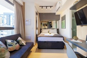 Habitación de hotel moderna con una cama grande, un sofá, un televisor y vistas a la ciudad.