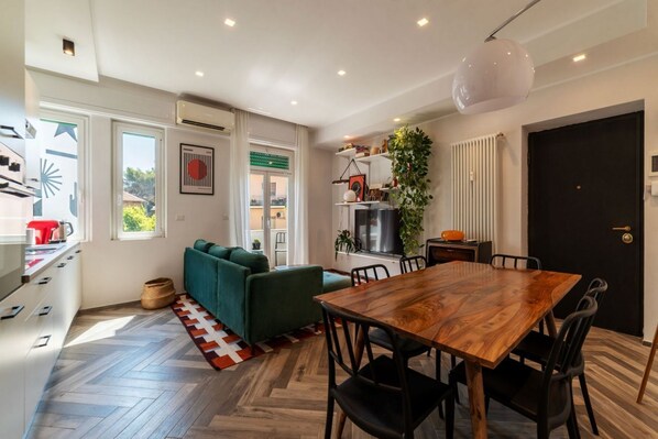 A modern kitchen with a dining area, a sofa, and a large window.