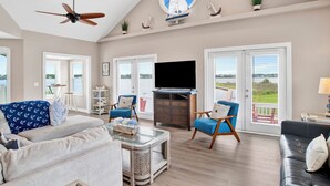 Un salon spacieux doté d’un ventilateur de plafond, d’un grand téléviseur et décoré avec des éléments rappelant le monde de la voile.