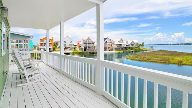 Une terrasse en bois blanche, d’où l’on peut admirer un lac et des maisons au loin.