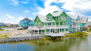 Une propriété située au bord de l’eau, avec plusieurs maisons peintes en vert et en bleu, une jetée et un petit bateau.