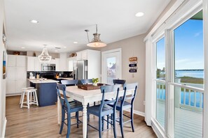 A modern kitchen with white cabinets, a central island, and a dining area with blue chairs. - Waterfront | Pet-Friendly | Private Pool, Boat Launch Access (Gulf Shores)