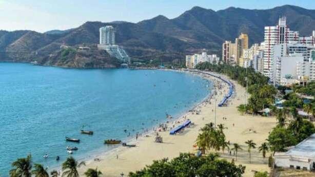 A coastal cityscape with a beach, buildings, and mountains in the background.