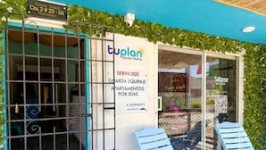 A building with a sign for 'tuplan Santa Marta' offering services like apartment rentals. There are two blue chairs outside.