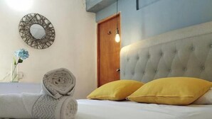 A neatly made bed with rolled towels and two yellow pillows, a round mirror on the wall, and a wooden door.