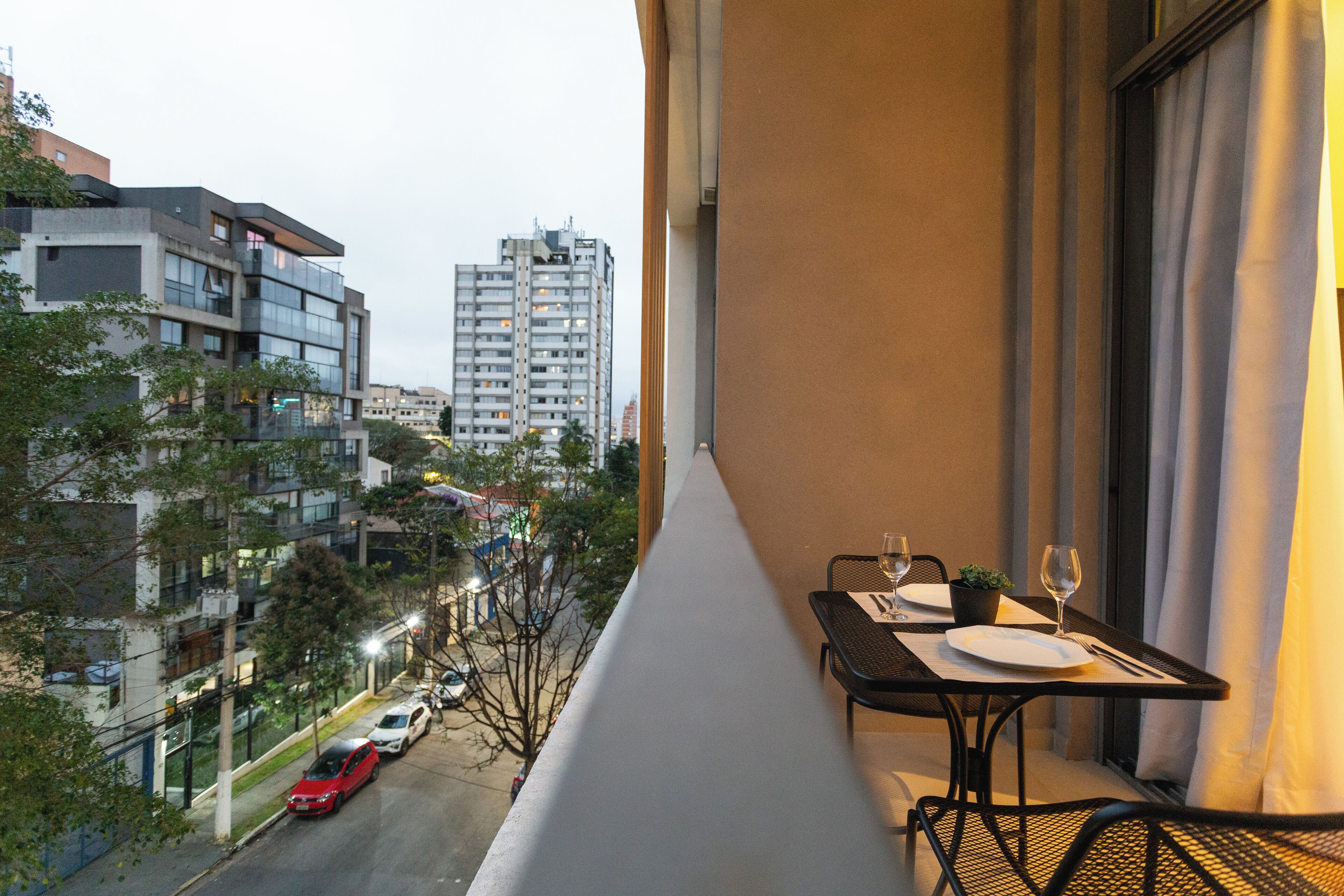 A balcony with a table set for two, overlooking a street with parked cars and buildings.