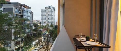 A balcony with a table set for two, overlooking a street with parked cars and buildings.