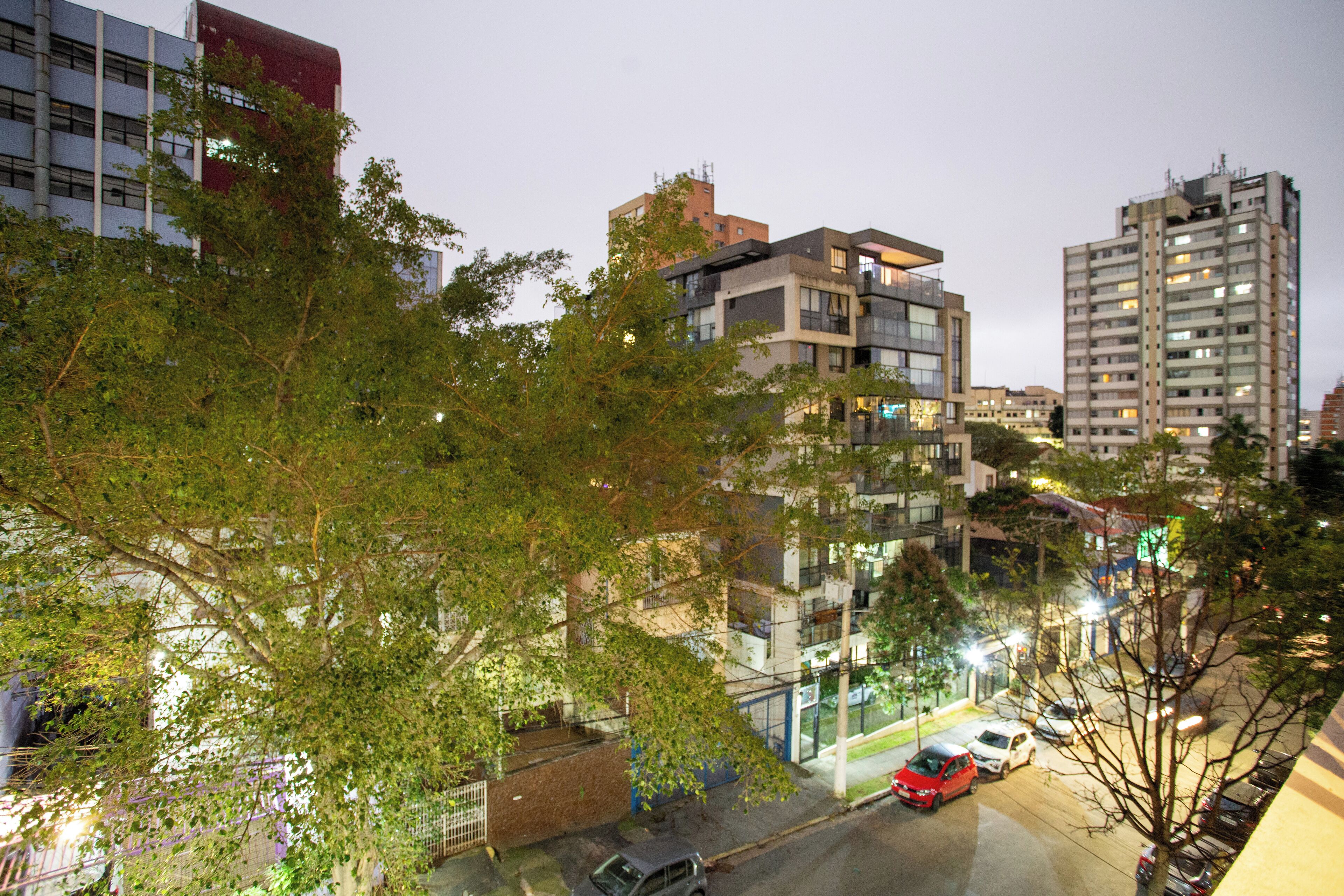 A multi-story residential building with balconies, a parking area, and trees in the foreground.