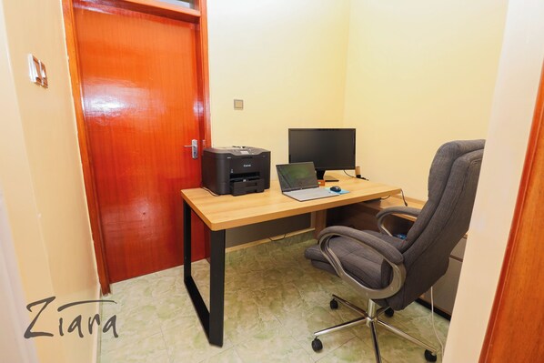 A small office space with a wooden desk, a laptop, a printer, and an office chair.