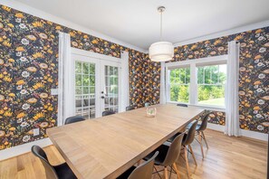 Une salle à manger avec une table en bois, des chaises noires, un luminaire suspendu et un papier peint à motifs floraux.