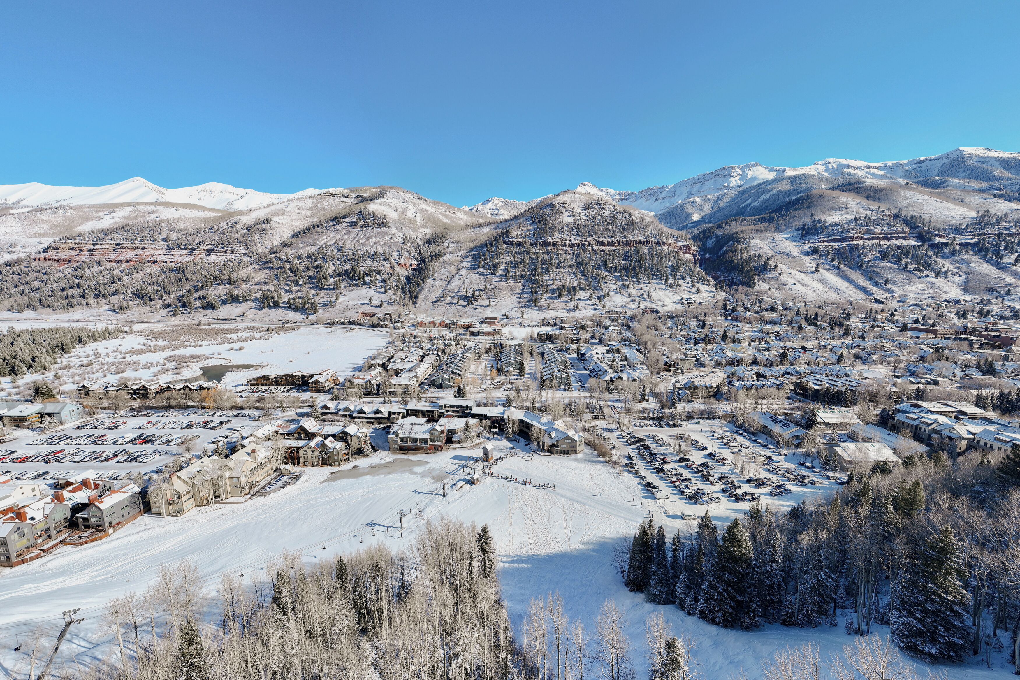 Un pueblo cubierto de nieve con edificios, una pista de esquí y montañas al fondo.