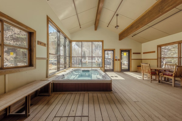 Un jacuzzi en una habitación con pisos de madera, ventanas amplias y techo de madera.