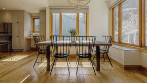 A dining area with a table and chairs, a chandelier, and large windows with a view of trees. - Cozy Mountain Condo by InvitedHome | In Town, Walkable to Ski / Shops (Telluride)