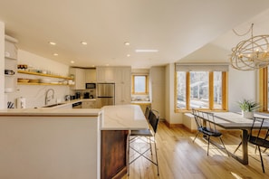 Una cocina moderna con armarios blancos, una isla de mármol y un comedor con mesa y sillas.