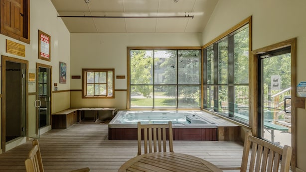 A wooden deck with a hot tub, wooden benches, and large windows offering a view of the outdoors. - Cozy Mountain Condo by InvitedHome | In Town, Walkable to Ski / Shops (Telluride)