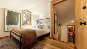 A bedroom with a bed, a wooden floor, a door, and a view of a kitchen. - Cozy Mountain Condo by InvitedHome | In Town, Walkable to Ski / Shops (Telluride)