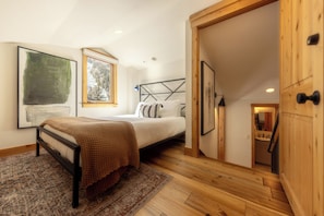 Un dormitorio con cama, piso de madera, una puerta y vistas a una cocina.