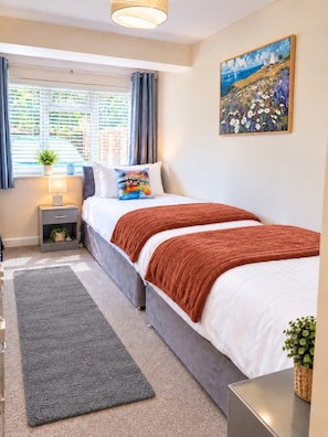 A bedroom with a bed, bedside table, lamp, curtains, and a painting on the wall.
