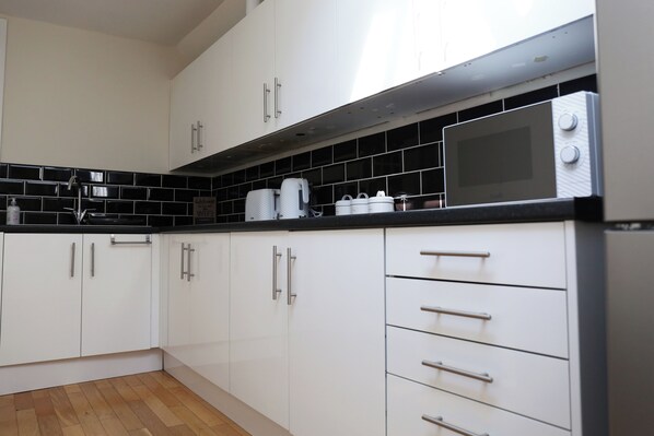 A modern kitchen with white cabinets, a black countertop, and a microwave.