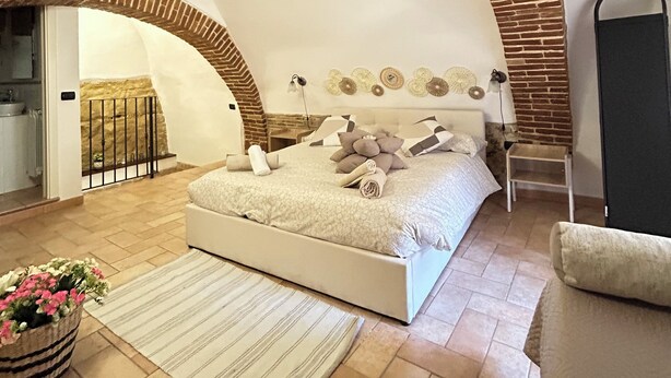 A bedroom with a vaulted ceiling, a bed with pillows and a rolled towel, a chair, a small table, and a potted plant. - The Bishop's Residence (Stimigliano)