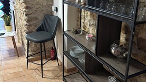 A room with a stone wall, a black metal shelf with glassware, a black chair, and a small potted plant. - The Bishop's Residence (Stimigliano)
