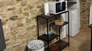 A kitchen with a stone wall, a clock, a microwave, a refrigerator, and a shelf with kitchen items. - The Bishop's Residence (Stimigliano)