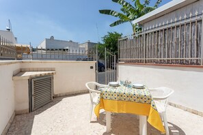 A patio with a table set for two, white chairs, and a yellow tablecloth.