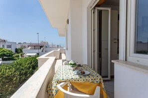 A balcony with a table set for two, a white chair, and a door leading to an interior room.