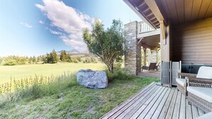A wooden deck with outdoor furniture, a stone wall, and a view of a grassy field and mountains. - Snowcreek Vi The Lodges #1197 3 Bedroom Condo (Mammoth Lakes)