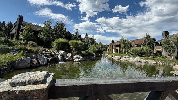A riverside view with a wooden bridge, stone rocks, and houses with a rustic architectural style. - Snowcreek Vi The Lodges #1197 3 Bedroom Condo (Mammoth Lakes)