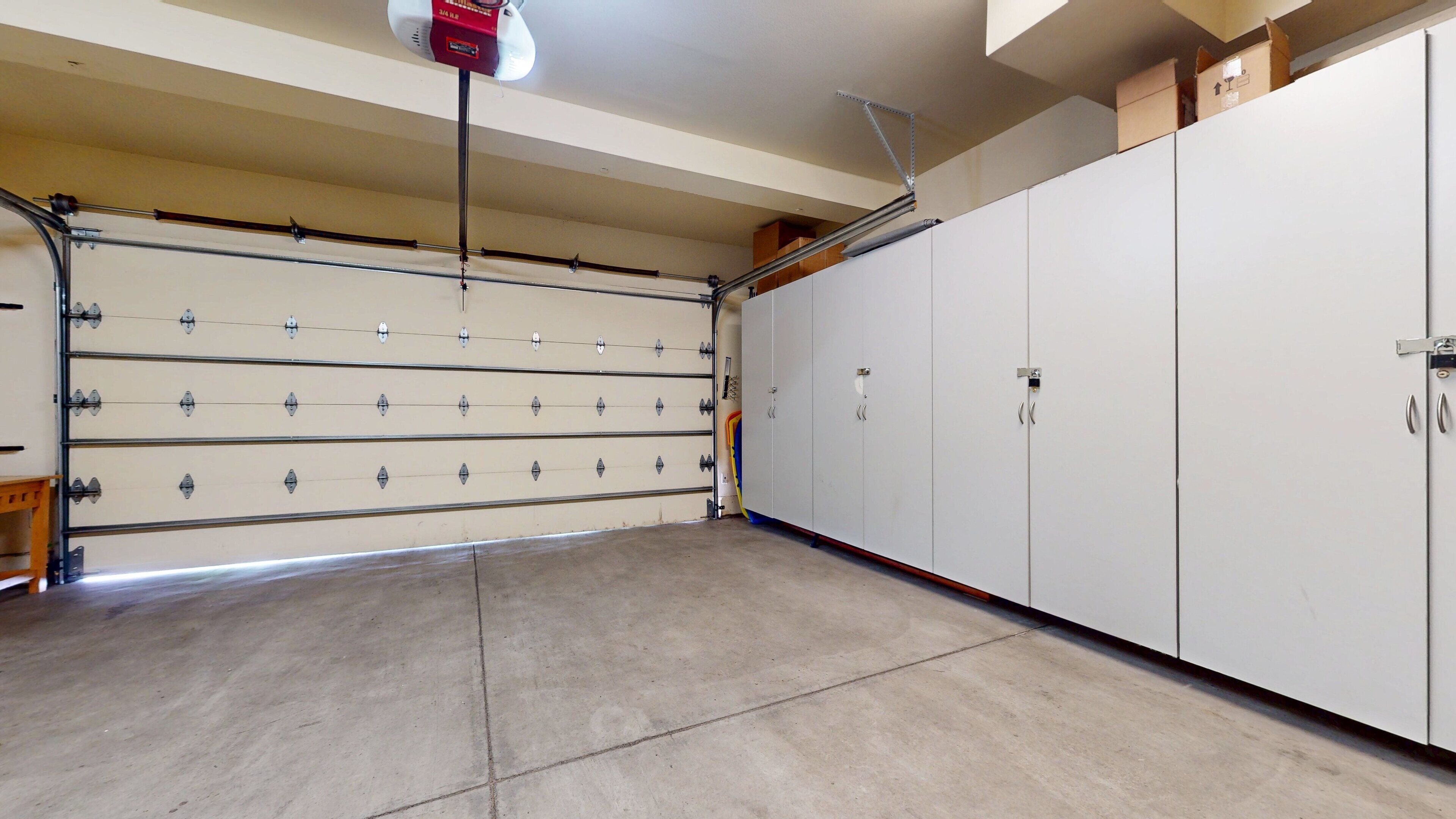 A garage with a large white garage door, multiple storage cabinets, and a ceiling fan.