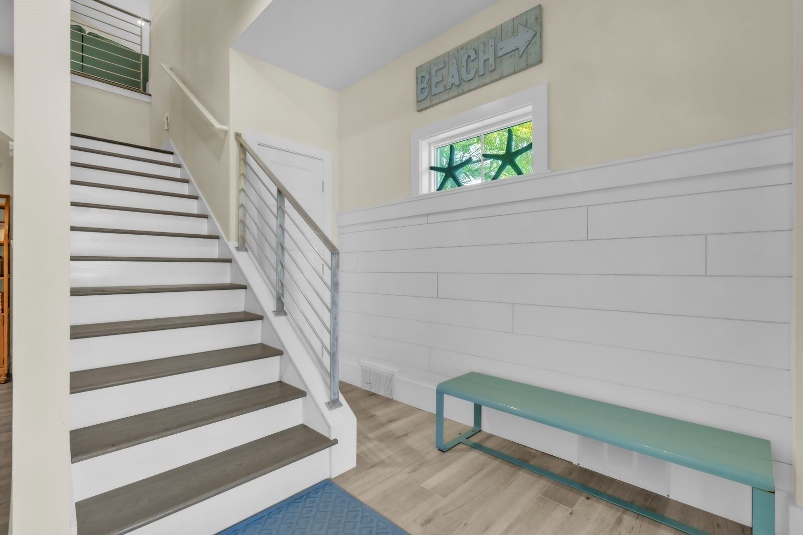 A staircase with a handrail, a bench, and a wall with a window and a sign.
