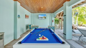 A pool table in a room with light green walls, wooden ceiling, and a television mounted above it. - Jersey Gal 3 Bedroom Home (Anna Maria)