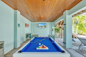 A pool table in a room with light green walls, wooden ceiling, and a television mounted above it. - Jersey Gal 3 Bedroom Home (Anna Maria)