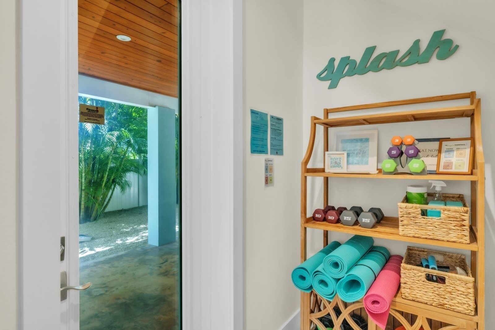 A hallway with a wooden shelf displaying yoga mats, dumbbells, and a small framed picture.