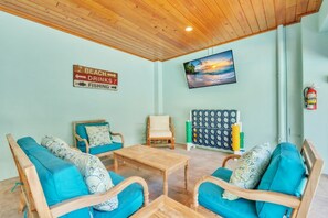 Een kamer met een houten plafond, een aan de muur bevestigde televisie, een bord waarop voorzieningen staan zoals strand, drankjes en vissen, en een brandblusser aan de muur.
