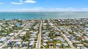 An aerial view of a coastal residential area with houses, roads, and a bridge in the distance. - Jersey Gal 3 Bedroom Home (Anna Maria)