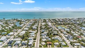An aerial view of a coastal residential area with houses, roads, and a bridge in the distance. - Jersey Gal 3 Bedroom Home (Anna Maria)